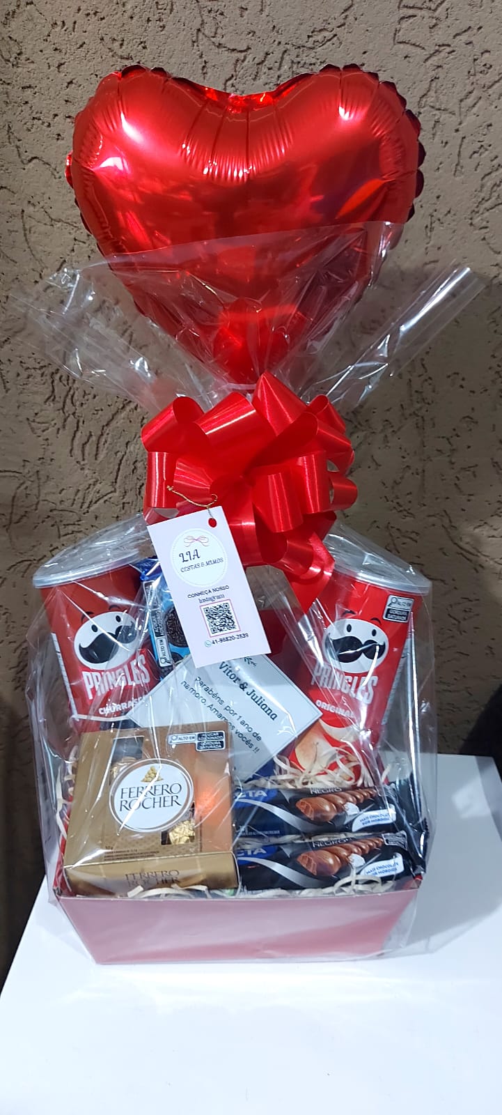 Cesta para presente, com um balão de coração vermelho, várias batatas pringles, chocolates.